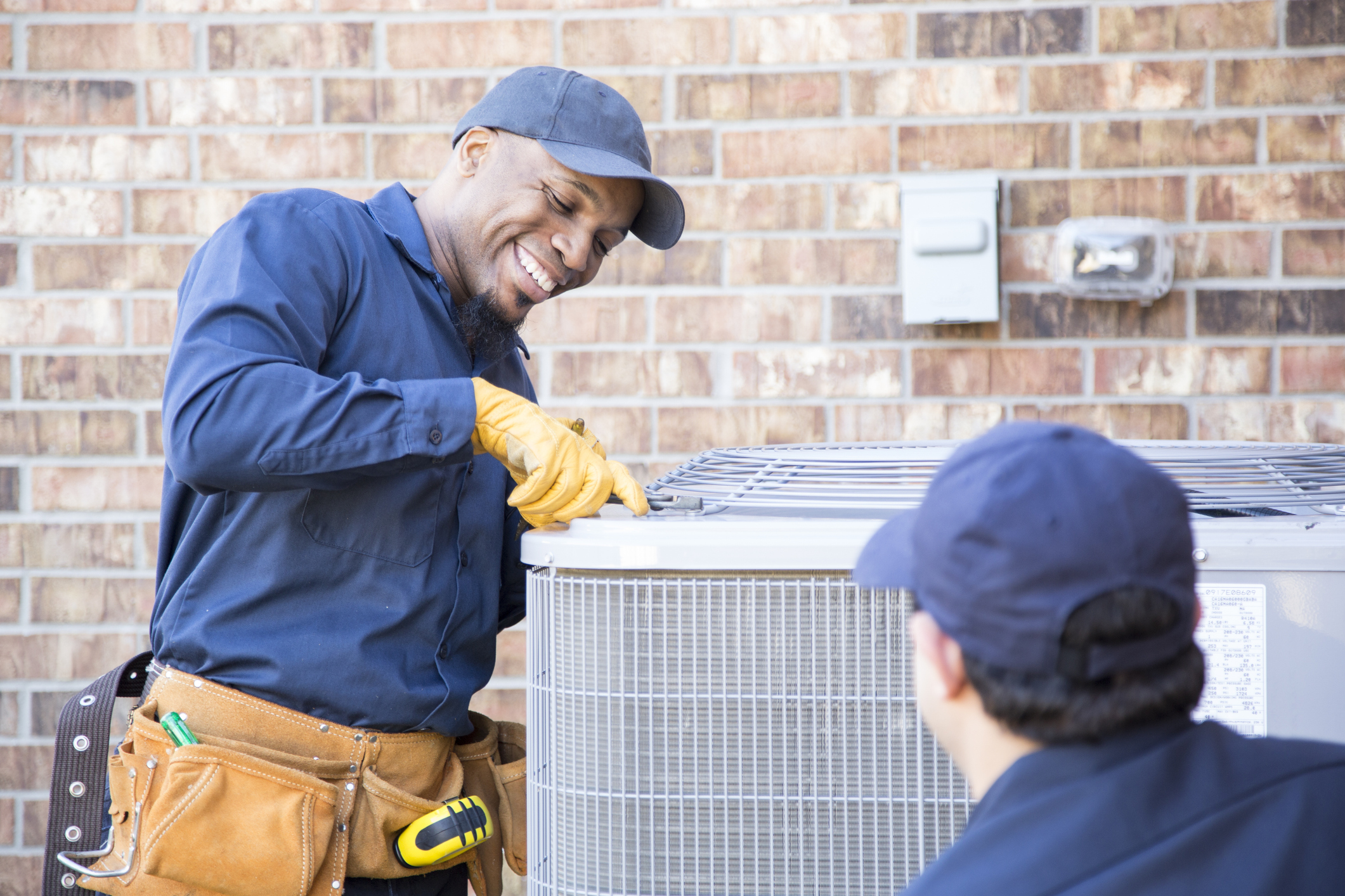 Multi-ethnic team of blue collar air conditioner repairmen at work. They prepare to begin work by gathering appropriate tools from their tool box.